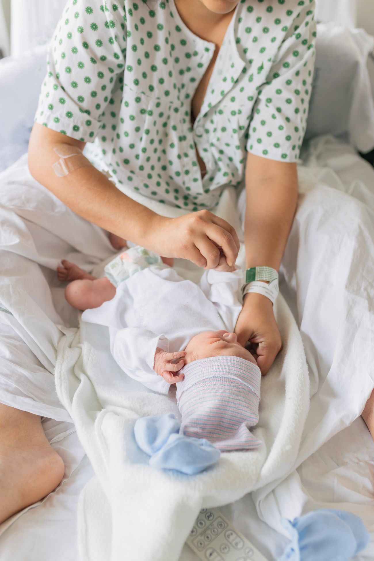 A mother in a hospital gown dressing her newborn