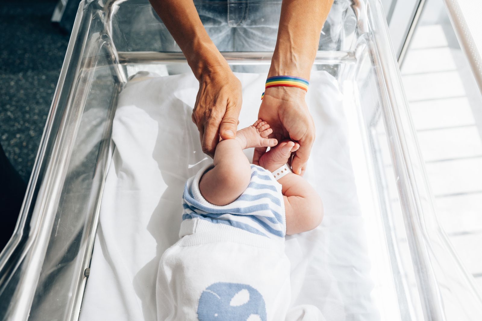 A newborn's feet held in an adult's hand in a hospital bed